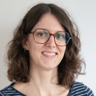 Frau mit braunen Locken, Brille und Lächeln.